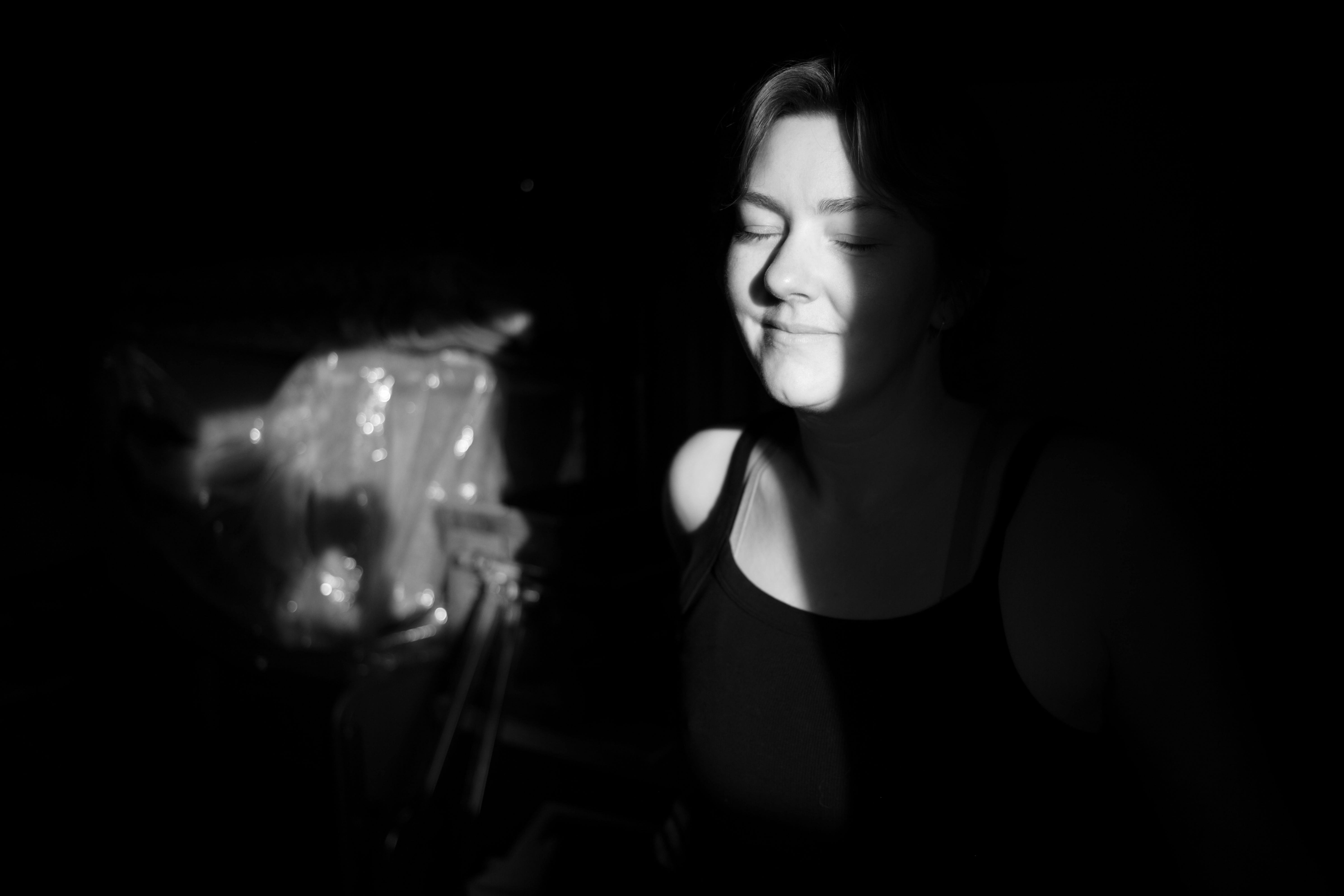 Someone stands, their face half in darkness, with a gentle smile